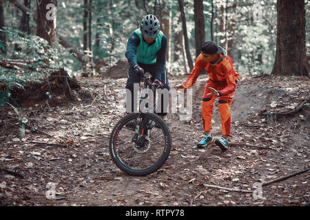 Moskau, Russland - Nov, 2018: MTB-Lehrer helfen Reiter lernen, Fahrrad zu fahren. Lehre ein Reiter, ein Fahrrad auf einem Trail zu fahren. Zwei Freunde haben Spaß in der Natu Stockfoto