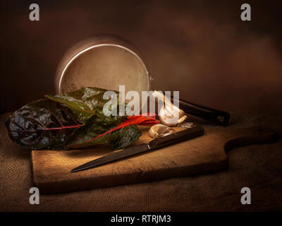 Ruby aka Mangold Gemüse Lebensmittel vorbereitung, Stillleben mit Knoblauch. Chiaroscuro stil Licht Malerei. Beta vulgaris. Stockfoto