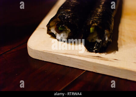 In der Nähe von zwei Sushi Rollen auf einer Holzplatte auf einem Holztisch Stockfoto