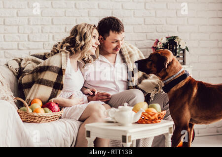 Junges Ehepaar mit ihrem Haustier am Morgen sitzen in einem gemütlichen Wohnzimmer Stockfoto
