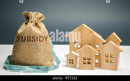 Geld beutel mit dem Wort Subvention und Holzhäuser. Finanzielle Hilfen, die Unterstützung der Bevölkerung. Finanzielle Beihilfen, zinslose Darlehen. Steuervergünstigungen, Versicherung, Stockfoto