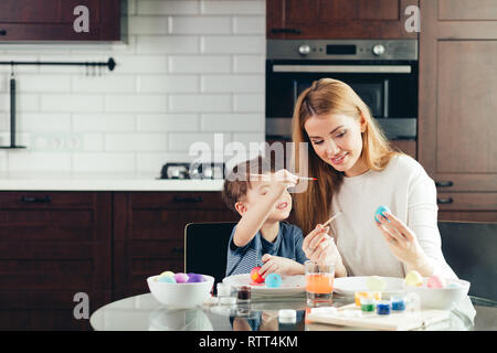 Glücklich liebende Familie von Mutter und Sohn vorbereiten Ostern Dekorationen. Mutter und Kind Junge sind, gekochte Eier mit bunten Farben und Spaß haben Stockfoto