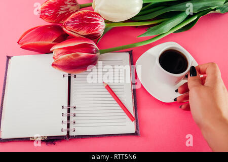 Frau, esspresso Kaffee und Verfassen von Notizen mit frischen Tulpen auf rosa Hintergrund. Beim Frühstück, während Sie Notizen Stockfoto