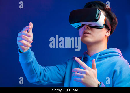 Freudige Japanische youngster Videospiel spielen in der virtuellen Realität Helm auf dunkelblauem Hintergrund. Smartphone mit Virtual reality Brillen. Technologien Stockfoto