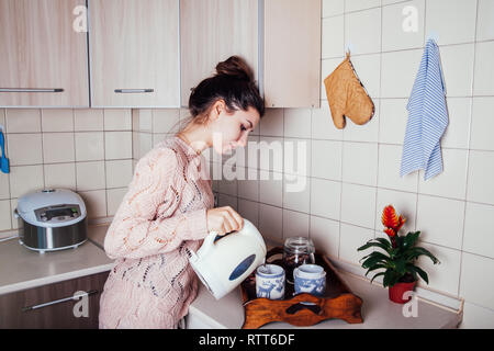 Junge Frau bereitet Tee für zwei in der Küche. Gießt Wasser in eine Tasse. Stockfoto