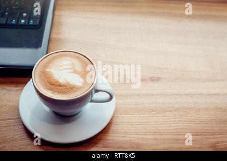 Kaffee trinken, während Sie mit einem Laptop im Cafe. Tasse Kaffee mit Laptop im Font des Fensters auf hölzernen Tisch. Stockfoto