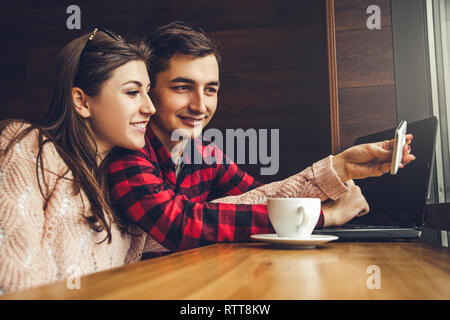 Junge paar nimmt selfie und genießt Kaffee im Cafe mit einem Laptop vor dem Fenster Stockfoto