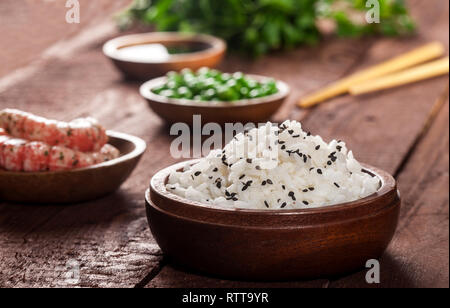 Gekochter weißer Reis in Houten mit Krabben, Erbsen, Sesam und Essstäbchen auf einem braunen Hintergrund. Stockfoto