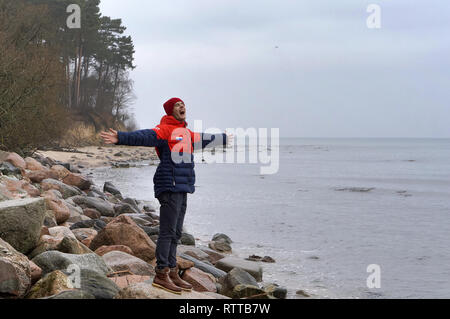 Junger Mann genießt das Meer, Regen und bewölkt am Meer, Ostseeküste, der Region Kaliningrad, Russland, 30. Dezember 2018 Stockfoto