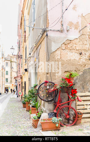 Alghero, Sardinien, Italien - Dezember 28, 2019: Bunte rote Rad mit Blumen auf der Straße von Alghero, Insel Sardinien in Italien Stockfoto