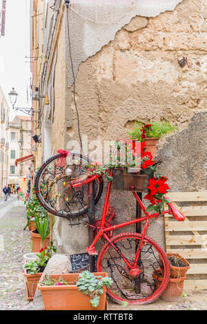 Alghero, Sardinien, Italien - Dezember 28, 2019: Bunte rote Rad mit Blumen auf der Straße von Alghero, Insel Sardinien in Italien Stockfoto