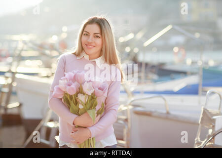 Schöne Mädchen im Frühjahr oder Herbst, durch das Meer im Boot Bucht. Mit einem Blumenstrauß in der Hand und engen stylischen Jeans und einen rosa Pullover Stockfoto