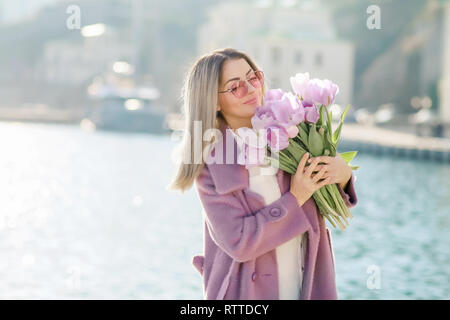 Schöne Frau mit glattes Haar mit einem Bouquet von rosa Tulpen eine Feder sonnigen Tag. Stockfoto