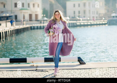 Schöne Frau mit glattes Haar mit einem Bouquet von rosa Tulpen eine Feder sonnigen Tag. Stockfoto