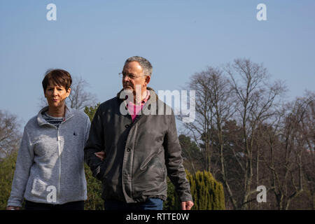 Entspanntes Paar, das an einem sonnigen Wintertag im Februar Arm in Arm durch einen öffentlichen Park geht, Harrogate, North Yorkshire, England, Großbritannien. Stockfoto