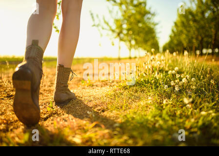 Blick auf Beine und Schuhe von gehen Mädchen in der Green Orchard durch den Pfad, während sonniger Tag. Stockfoto