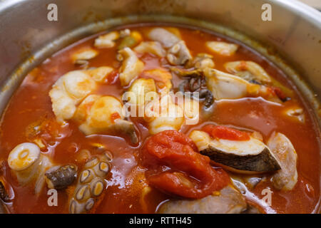 Kochende Brühe mit Tomaten und Tintenfisch im Kochtopf Stockfoto