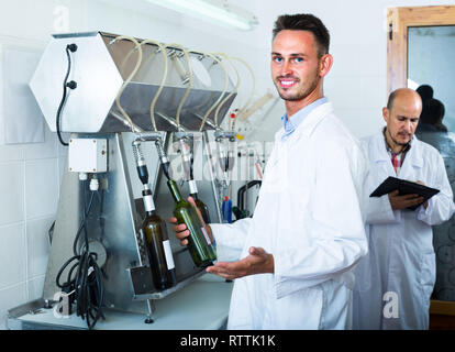 Portrait der junge lächelnde männlichen Weingut Arbeiter mit der Abfüllung von Maschinen im Werk Stockfoto