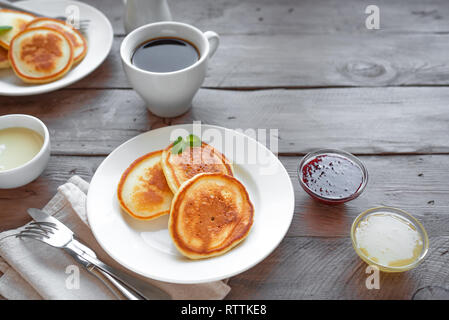 Pfannkuchen zum Frühstück. Hausgemachte Pfannkuchen mit verschiedenen Toppings, Marmelade, Honig und Kaffee auf Holztisch, kopieren. Stockfoto
