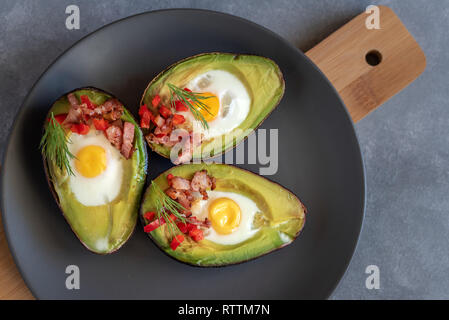 Wachteleier in Avocado mit Speck gebraten, rote Paprika und Dill. Stockfoto