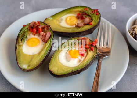 Wachteleier in Avocado mit Speck gebraten, rote Paprika und Dill. Stockfoto