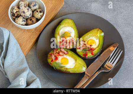 Wachteleier in Avocado mit Speck gebraten, rote Paprika und Dill. Stockfoto