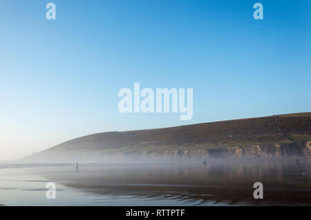 Surfer am Strand in der Sonne an einem warmen Februar Tag Silhouette. Saunton, Devon, 27. Feb 2019. Stockfoto