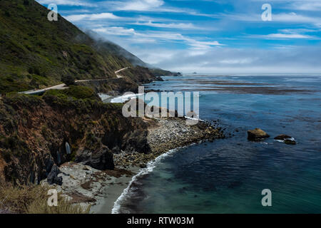 Die zerklüftete Küste von Big Sur, CA mit dem highway Weben und umarmen die Hügel mit Blick auf das Meer, den schönen blauen Himmel Stockfoto