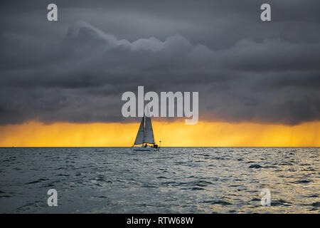 Lonely Segelboot in den Ozean vor der herannahenden Sturm und dunkle Wolken mit einem sunrise Licht, Englischer Kanal, in der Nähe von Frankreich Stockfoto
