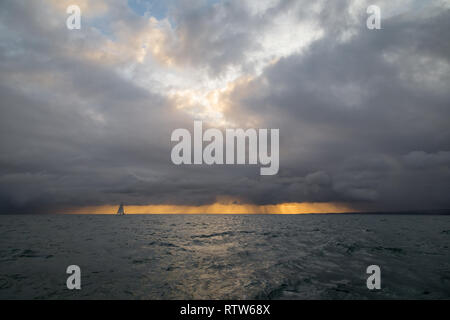 Lonely Segelboot in den Ozean vor der herannahenden Sturm und dunkle Wolken mit einem sunrise Licht, Englischer Kanal, in der Nähe von Frankreich Stockfoto