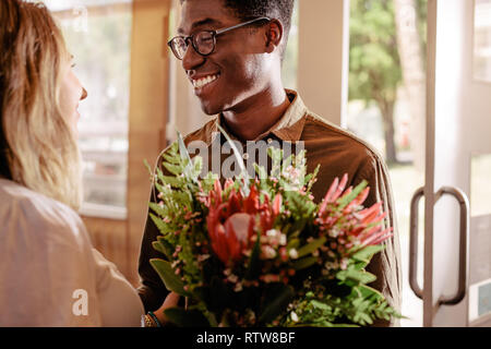 Junge afrikanische Mann mit Blumen treffen seine Freundin. Mann gibt der Blumen in das geliebte Mädchen auf Datum. Stockfoto