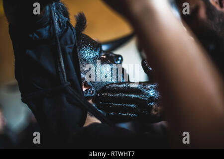 Ein Nachtschwärmer ist, mit Öl und Ruß während der Teufel von Luzon Karneval. Hunderte von Menschen aus der alten Tradition des Festivals der Teufel und die maskierten Figuren zu feiern. Leute kleiden wie Teufel mit Stier Hörner, Kuhglocken und Malen thei Körper mit schwarzen Öl und Ruß. Nachtschwärmer tragen weiße Masken. Die Tradition geht zurück bis in das 14. Jahrhundert. Stockfoto