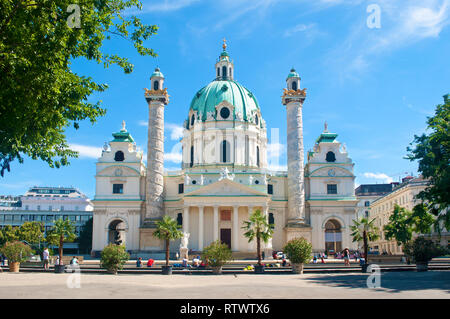 Fassade der Karlskirche (St. Charles Kirche) gegen den blauen Himmel und weißen Wolken an einem heißen Sommertag. Mehrere Töpfe mit Palmen und Büschen st Stockfoto