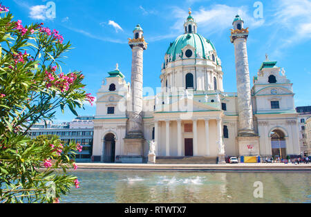 Fassade der Karlskirche (St. Charles Kirche) gegen den blauen Himmel, weiße Wolken und ein Teich mit Wasser spritzt an einem heißen Sommertag. Green Tree Branch mit Stockfoto