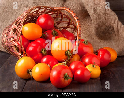Rote und gelbe Tomaten in einem Weidenkorb auf hölzernen Tisch Stockfoto