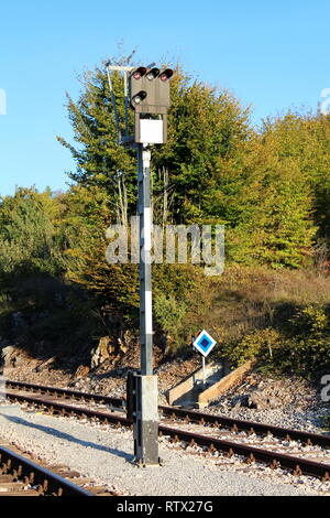 Schwarze und weiße hohen Metallmast mit Railway signal Lichter auf umgeben mit Kies und Bahnstrecken mit dichten Bäumen und strahlend blauer Himmel Stockfoto