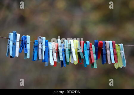 Bunte Wäscheklammern aus Kunststoff in verschiedenen Größen und Formen dicht auf einem Seil nass vom Regen auf dunklen regnerischen Nachmittag Stockfoto