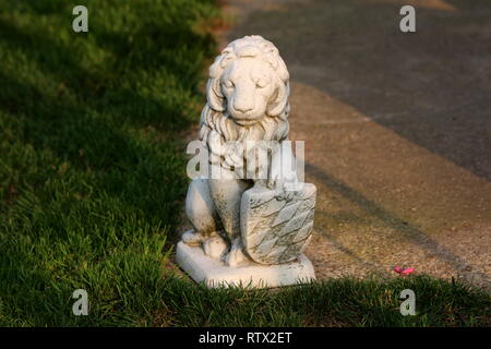 Beton Skulptur von mighty Lion holding Schild am Rande von konkreten Weg mit Gras auf warmen sonnigen Tag bei Sonnenuntergang umgeben Stockfoto