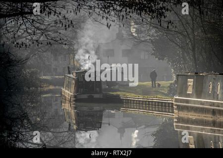 Einem nebligen Morgen auf der Trent und Mersey Canal an Great Haywood in Staffordshire. Die Szene zeigt Dog Walker und ein Boot mit Rauch aus dem Schornstein Stockfoto