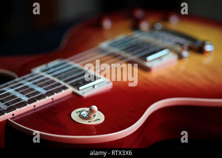 Nahaufnahme des Rhythmus und Höhen Switch auf einer neuen Cherry Red E-Gitarre mit Streichern im Hintergrund Stockfoto