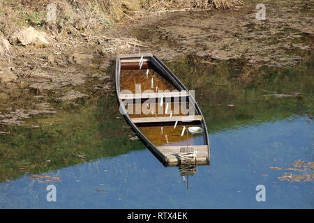 Teilweise eingetaucht alten hölzernen River Boat nächsten Ufer mit schwimmenden Gras und klares Wasser auf warmen sonnigen Tag umgeben zu Schlammigen Stockfoto