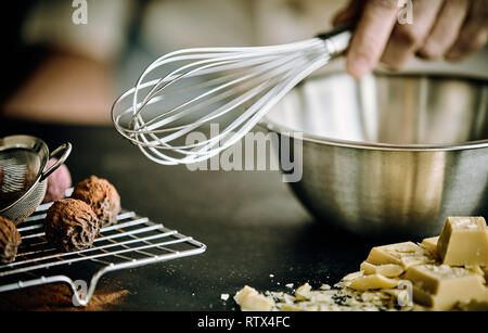 Hand ein Chef mit einem alten Metall über einen Schneebesen aus Edelstahl Schüssel mit Schokolade Bonbons neben Stockfoto