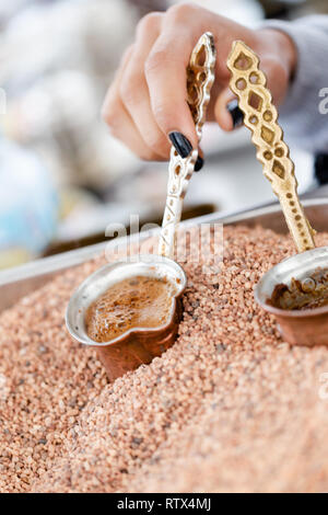 Traditionellen türkischen, arabischen Kaffee in kleinen Kupfer cups im heißen Sand gebraut. Nahaufnahme Stockfoto