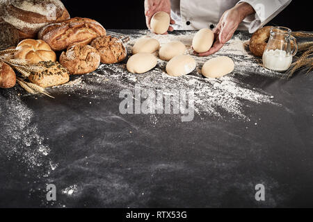 Bäcker oder Koch, die Brötchen aus rohen Teig auf einer Mehl Bäckerei Zähler mit einer Anzeige der seine Spezialität Brot zur Seite Stockfoto