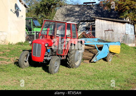 Red Tractor neben Familie Haus mit alten landwirtschaftlichen Geräte im Hintergrund mit Scheune und andere Traktor im Hintergrund umgeben geparkt Stockfoto