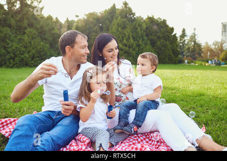 Glückliche Familie hat Spaß mit Seifenblasen auf dem Rasen im Park. Stockfoto