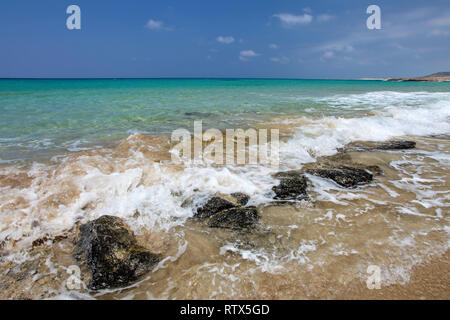 Kleine Wellen brechen am schwarzen Felsen am sandigen Strand, schöne blaue kristallklare Wasser im Hintergrund. Karpass, Nordzypern Stockfoto