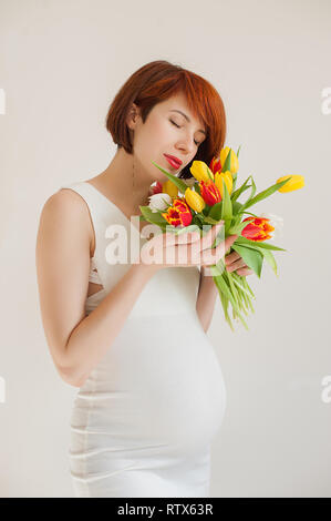 Glückliche junge schwangere Frau in weißem Kleid mit Blumen Stockfoto