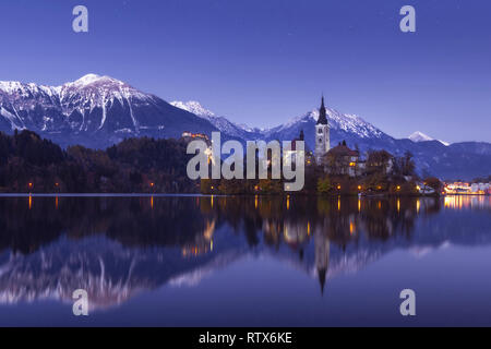 Malerischer Blick auf den See im Winter Nacht mit Castle Rock und St. Martin Kirche unter schöner Sternenhimmel im See Wasser spiegelt Bled Stockfoto