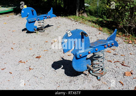 Zwei Vintage Retro alt draußen öffentlichen Spielplatz ausrüstung in Form von Pony Spring Rider schwingt mit Griffen und rissig verfallenen blaue Farbe Stockfoto